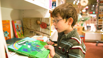 Ein kleiner Junge betrachtet in einem Buchladen ein Buch