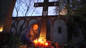 Junge Frau zündet Grablicht an einem Grab auf einem Friedhof an.