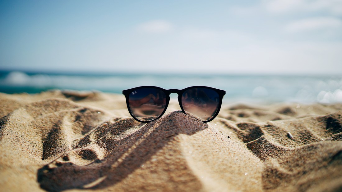 Sonnenbrille auf einem Strandhügel vor dem blauen Meer