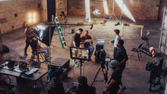 Filmset in Fabrikhalle mit Lampen, Kameras und Personen.