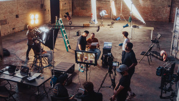 Filmset in Fabrikhalle mit Lampen, Kameras und Personen.