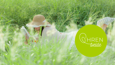 Junge FRau mit Hut liegt auf einer Sommerwiese und list