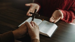 zwei Menschen diskutieren mit ihren Händen über einer Bibel und einem Kreuz