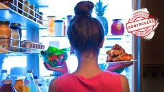 Frau steht vor Kühlschrank mit Gemüse und Fleisch in den Händen