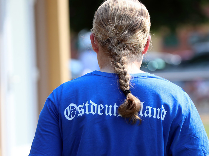 Junge Frau von hinten zu sehen, trägt ein blaues T-Shirt mit der Aufschrift 'Ostdeutschland'