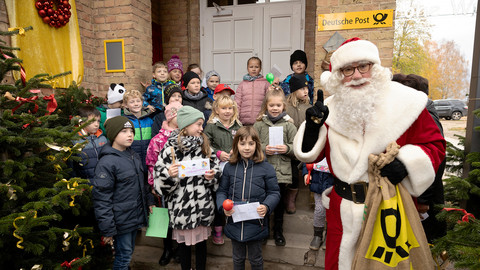 Vor der Weihnachtspostfiliale Himmelpfort steht der Weihnachtsmann umgeben von Kindern