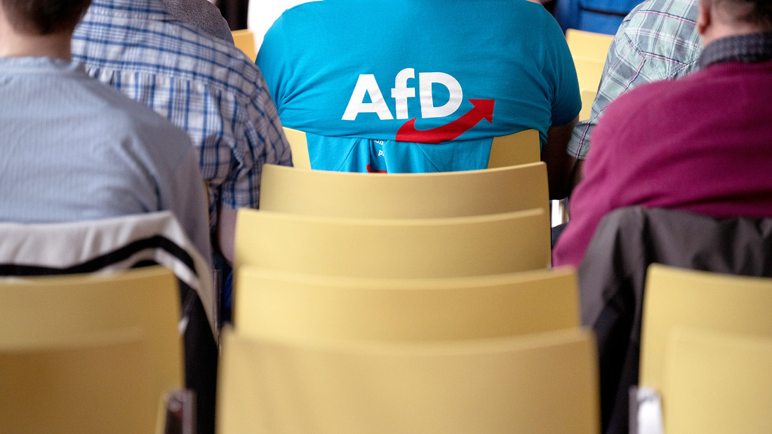 Mann mit AFD T-Shirt, von hinten gesehen, sitzt auf einem Stuhl.