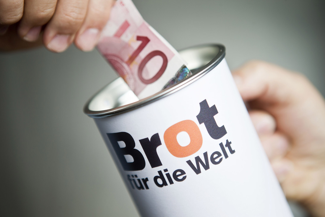 Brot für die Welt Spendendose und Hand mit zehn Euro Schein