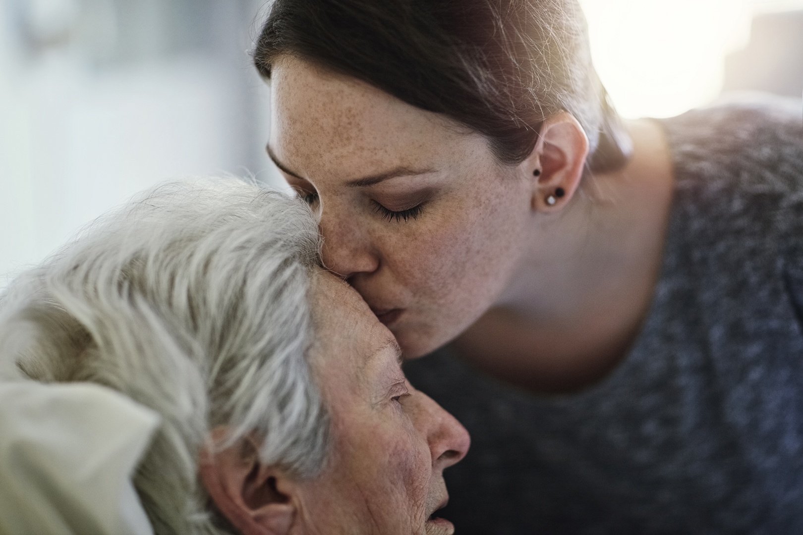 Tochter küßt alte Mutter im Bett