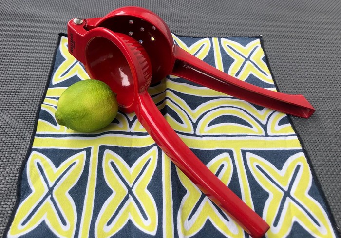 Rote Zitronenpresse mit Limone auf Tischdecke 