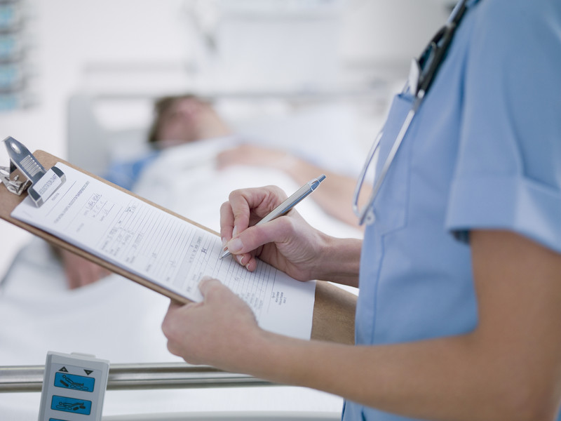 Krankenschwester vor einem Patientenbett mit Anamese-Protokoll