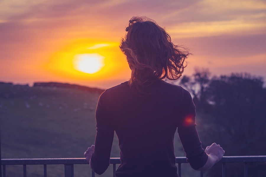 Frau blickt von Balkon in die aufgehende Sonne