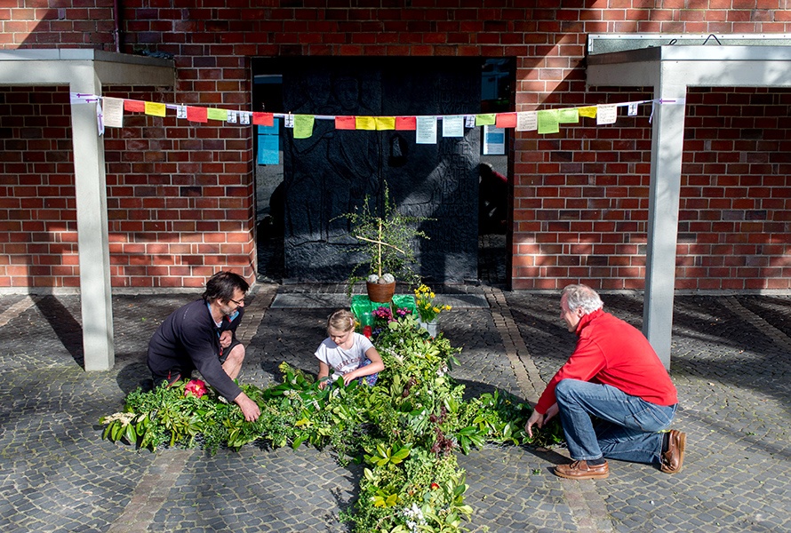 Besucher stecken grüne Zweige in ein Maschenkreuz vor der St.-Johannes-Kirche im Oldenburger Stadtteil Kreyenbrück. 