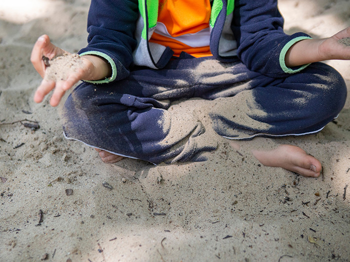 Kind mit Jogginghose sitzt im Schneidersitz im Sand