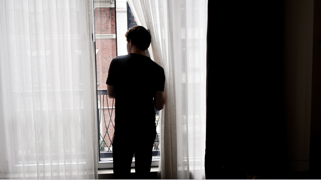Junger Mann steht sehnsüchtig am Fenster und blickt nach draußen