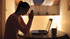 Trauernde Frau mit gefalteten Händen vor dem Laptop