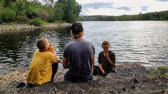 Drei Menschen sitzen auf Steinen an einem See.