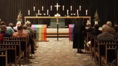 Foto zeigt einen CSD-Gottesdienst - Blick nach vorn zum Altar, vor dem Regenbogenflaggen drapiert sind. Besucher sitzen links und rechts auf den Kirchenbänken
