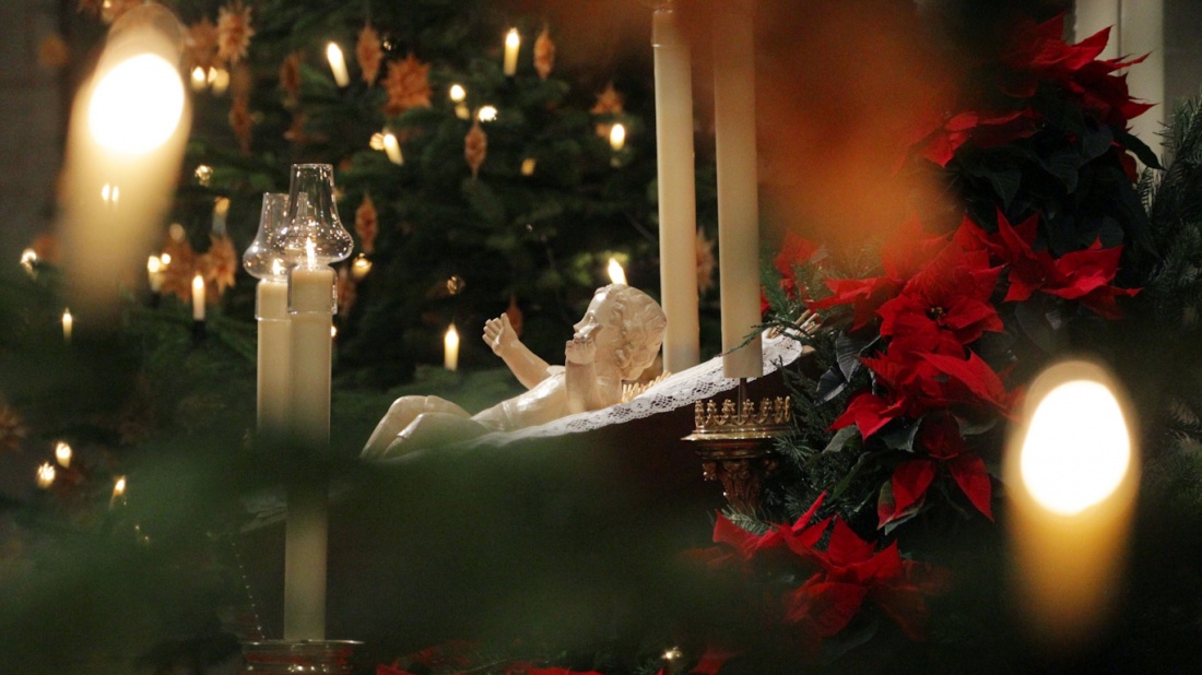Eine Jesuskrippe zwischen Weihnachtsstern,  Tannenzweigen und Kerzenlicht.