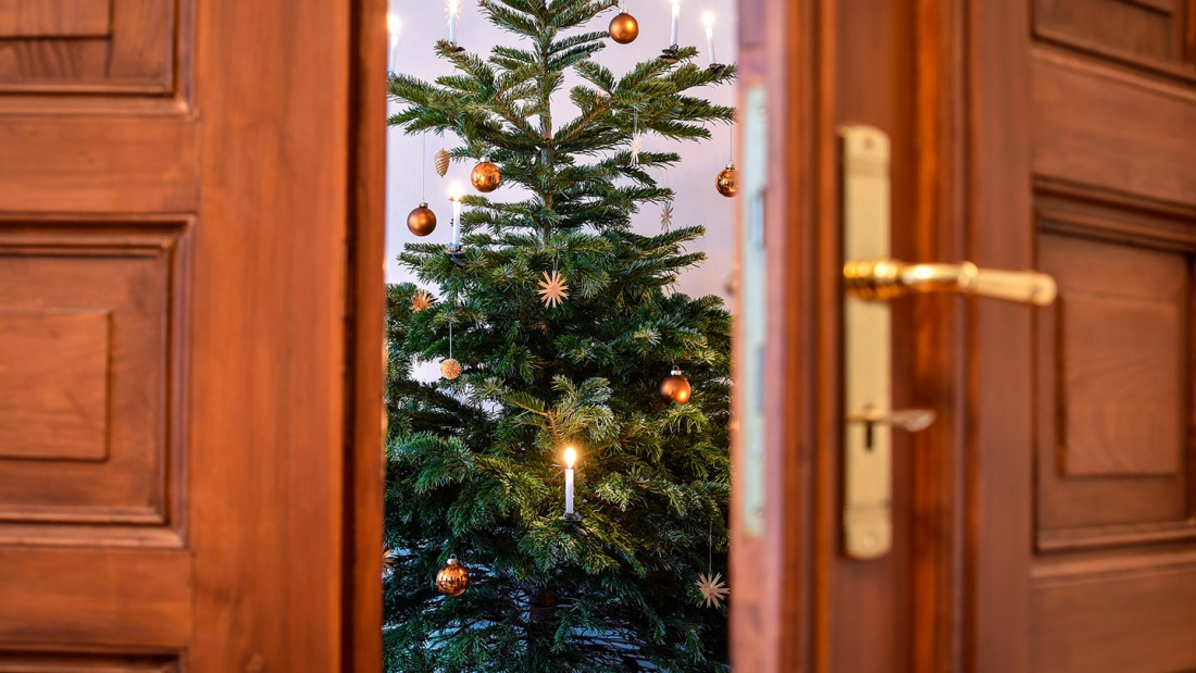 Blick auf einen geschmückten Weihnachtsbaum durch eine geöffnete Tür