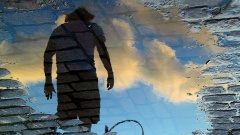 Ein Mann spiegelt sich in einer Pfütze auf der Straße.