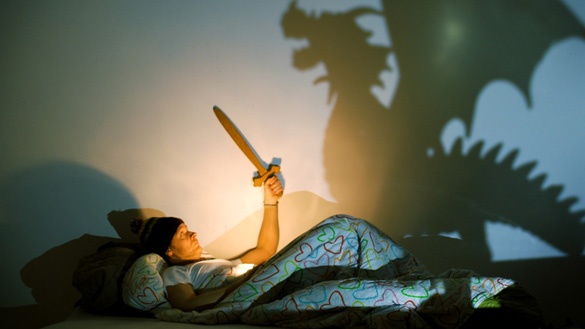 Mann liegt im Bett und bekämpft Schatten-Drache mit Schwert.