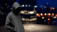 Ein Mann steht im Dunkeln und verbirgt sein Gesicht unter einer Kapuze.