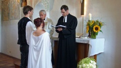Brautpaar steht in einer Kirche vor zwei Pfarrern.
