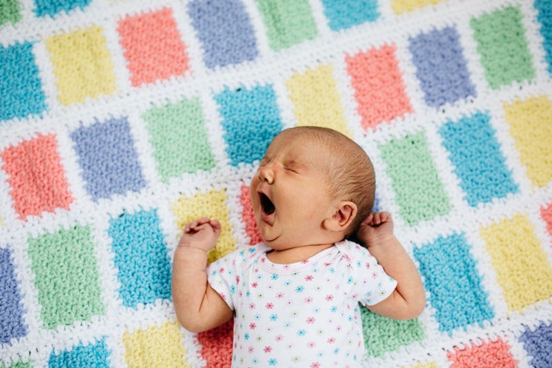 Baby liegt auf Babydecke. Es gähnt.