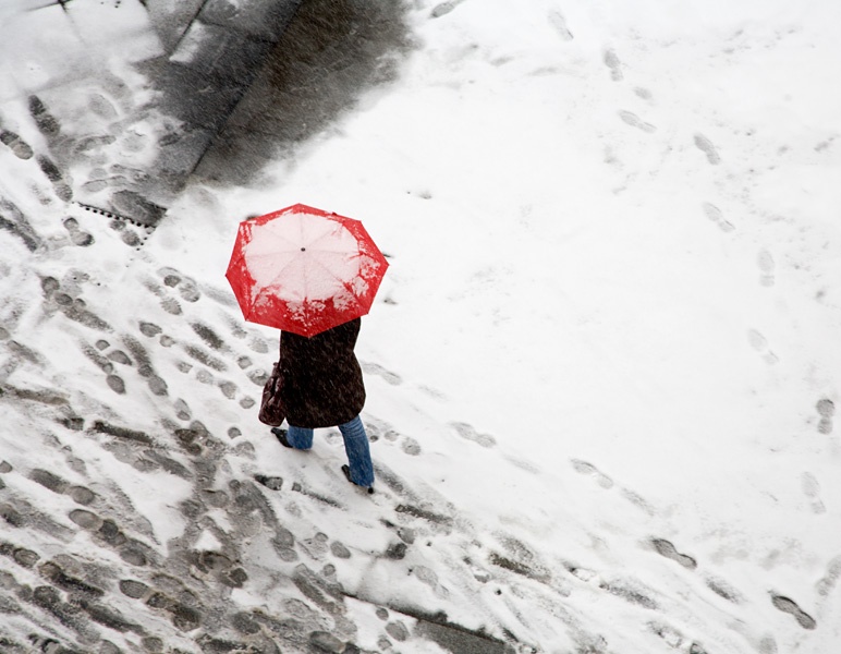 Eine Frau läuft mit einem roten Schirm durch den Schnee.