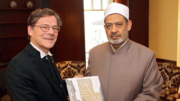 Bischof Markus Dröge überreicht dem Imam ein Buch über das Projekt des Drei-Religionen-Hauses in Berlin.