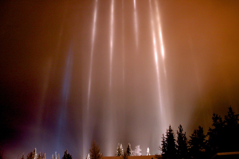 Lichtstrahlen fallen im Dunklen auf Dächer und Baumkronen.