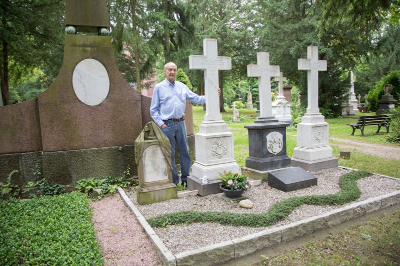 Dieter Georg umfasst das etwa zwei Meter hohe Kreuz auf dem Grab des Zappel-Philipp Urbilds von Fabricus. Auf dem Grab erinnern zwei weitere ähnliche Kreuze und ein kleineres an die Verstorbenen.