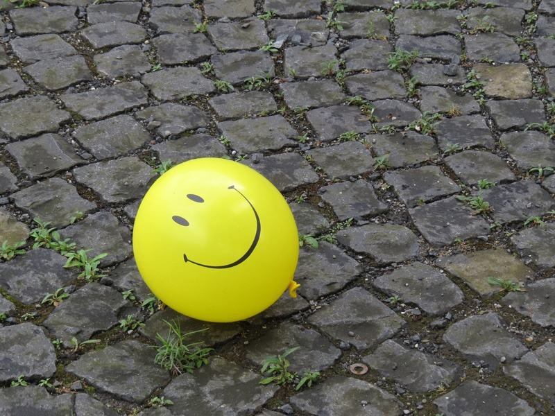 Ein Luftballon mit aufgedrucktem Smiley liegt auf Pflastersteinen. 