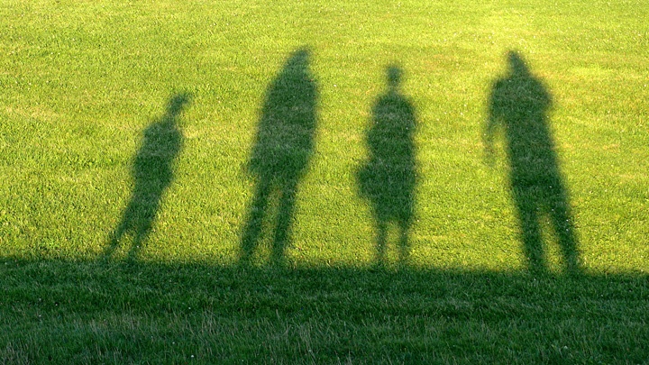 Schatten von zwei Erwachsenen und zwei Kindern auf einer Wiese.