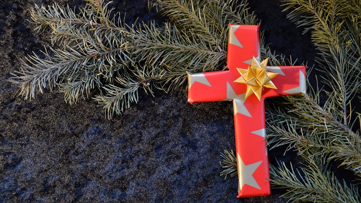 Ein Kreuz aus weihnachtlichem Geschenkpapier liegt auf einem Tannenzweig. 