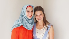 Eine Muslima und eine Christin stehen nebeneinander und lächeln in die Kamera.