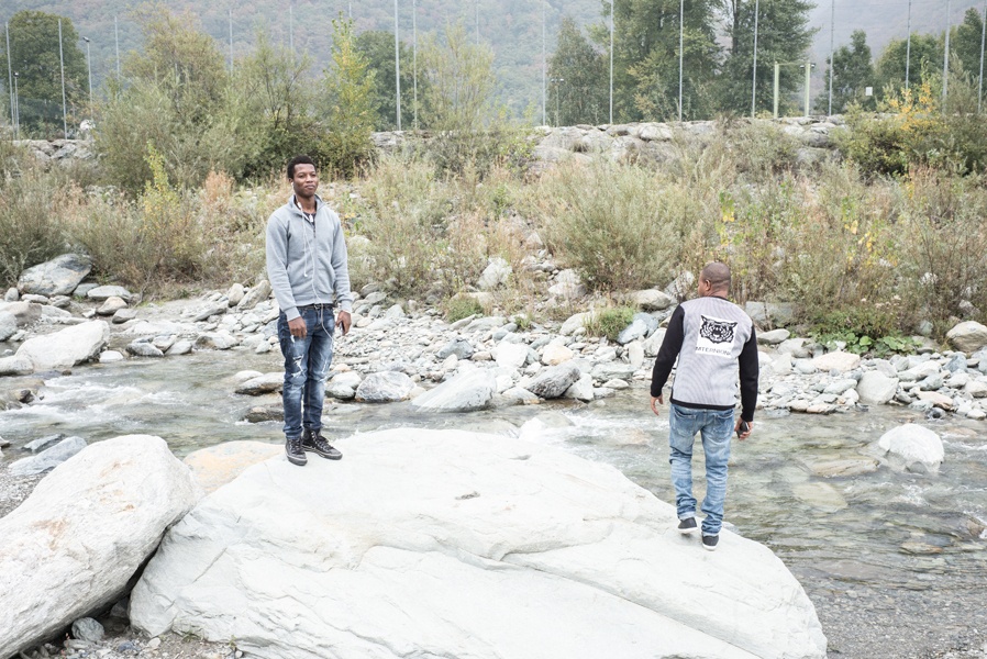 Zwei der jungen Männer stehen auf einem Felsen über einem Fluss, der Schnee ist abgetaut.