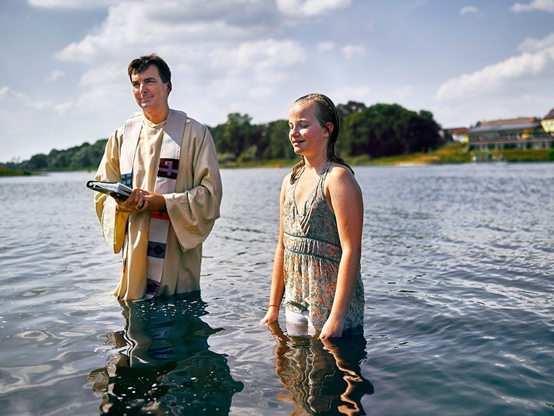 Ein Pastor und ein junges Mädchen stehen während der taufe im Wasser der Elbe
