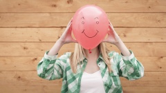 Eine junge Frau hält einen rosa Luftballon auf den ein Smiley gemalt ist vor ihr Gesicht.