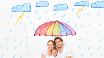 Vater, Mutter und Kleinkind sitzen vor einer Wand, auf die ein bunter Regenschirm und Regenwolken gemalt sind. 