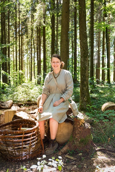 Wibke Kaese sitzt im Wald neben einem Holzkorb.