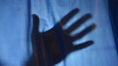 Der Schatten einer Hand zeichnet sich hinter einem Vorhang ab.