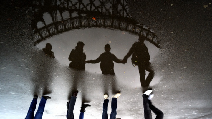 Vier Menschen spiegeln sich in einer Pfütze unter dem Eiffelturm in Paris.