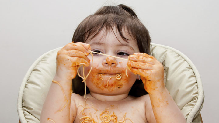 Kind mit verschmiertem Mund und Spaghetti in den Händen 