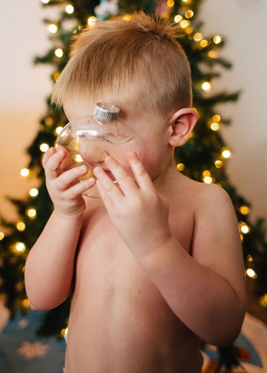 Junge steht vom Weihnachtsbaum mit Christkugel in der Hand.