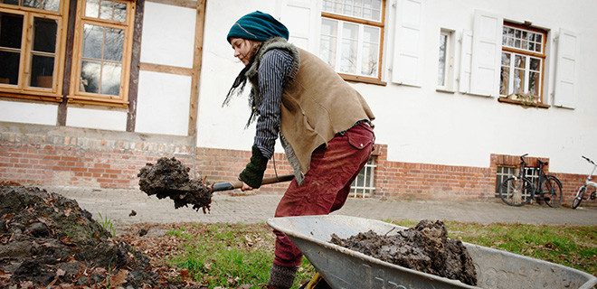 Die reisende Lehmbauerin Daria Anatzki schaufelt Naturlehm in eine Schubkarre. 