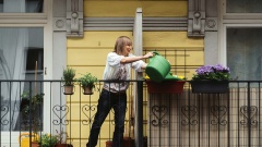 Frau gießt die Blumen ihrer Nachbarn von ihrem Balkon aus.