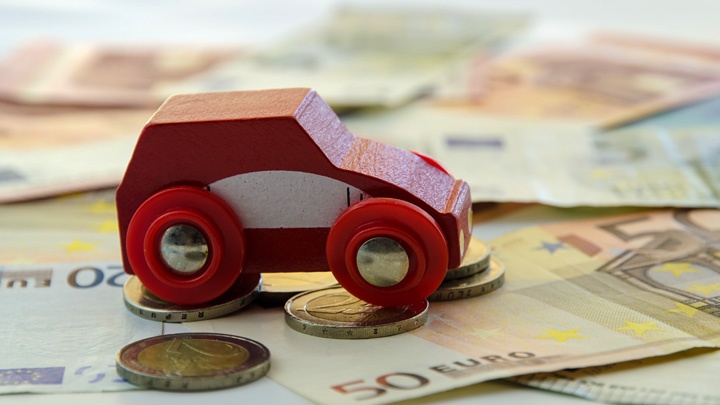 Ein rotes Spielzeugauto aus Holz steht auf Geldscheinen und Münzen.
