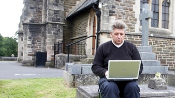 Pfarrer mit Laptop vor der Kirche